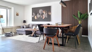 Un salon moderne avec un coin repas, comprenant un canapé, des fauteuils, une table et un grand tableau abstrait.