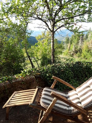 Un banc en bois avec des coussins à rayures, placé à l’extérieur, offrant une vue sur un paysage montagneux.