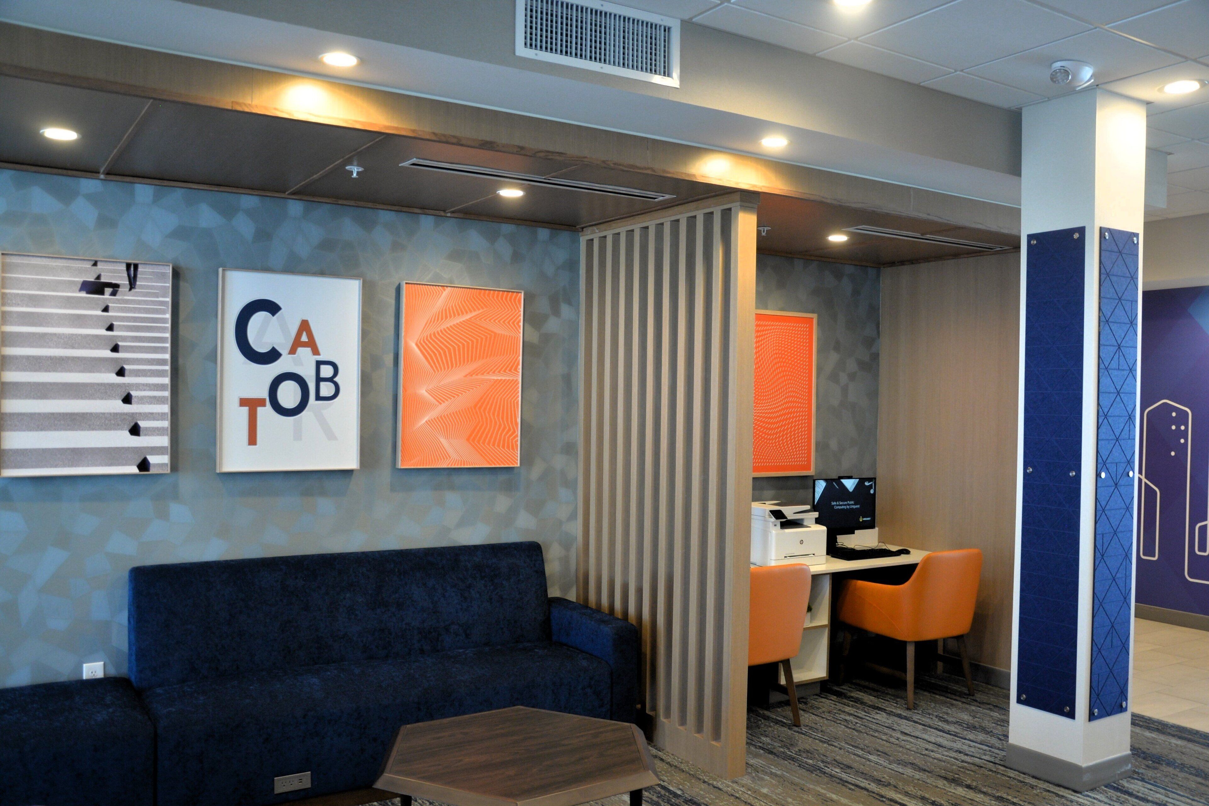 A modern hotel lobby with a blue sofa, a wooden coffee table, and a desk with an orange chair.