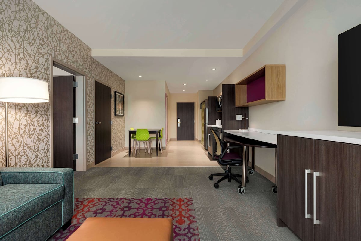 A modern hotel room with a sofa, a desk, a chair, and a small dining table.