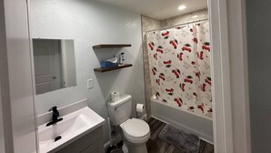 Ein Badezimmer mit weißem Waschbecken, Spiegel, Toilette und Duschvorhang mit festlichem Muster.