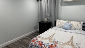 Ein Schlafzimmer mit einem Bett, einem Nachttisch, einer Wand-Klimaanlage und einem Fenster mit Vorhängen.