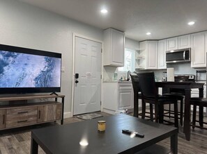 A modern kitchen with white cabinets, a microwave, and a dining area with a table and chairs. - Apartment San Isidro near UCDMC (Sacramento)