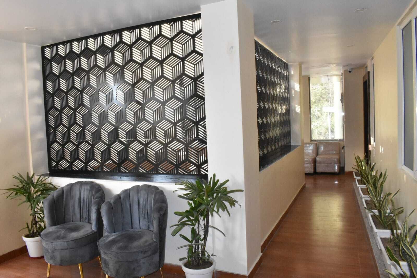 Un interior moderno con una pared de diseño geométrico, dos sillones tapizados en gris y plantas en macetas.