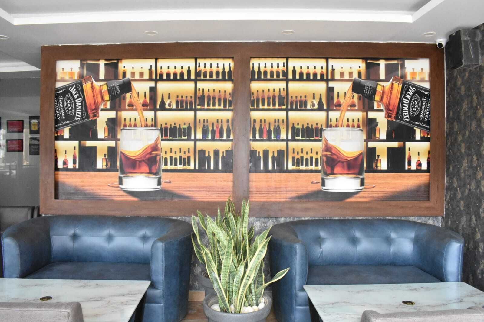 A bar area with two mirrored wall paintings of whiskey bottles and glasses, leather seating, and a potted plant.