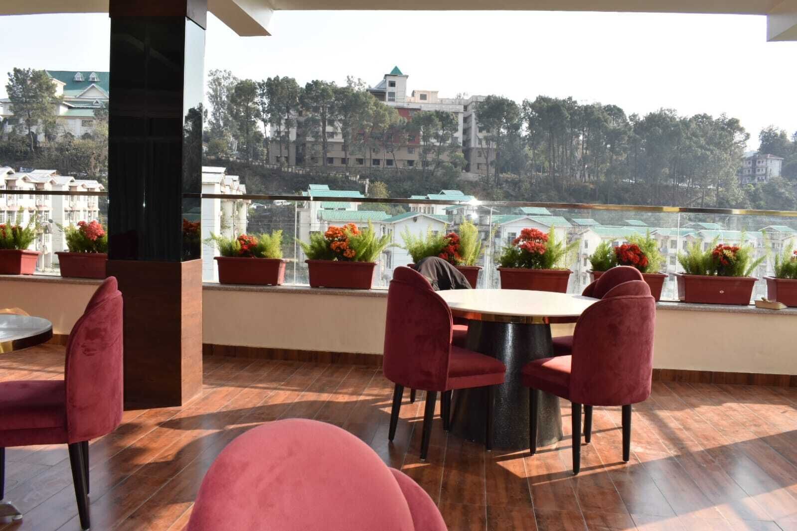 Una terraza con una mesa redonda y sillas rojas, rodeada de macetas con flores rojas.