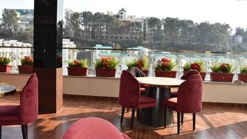 Una terraza con una mesa redonda y sillas rojas, rodeada de macetas con flores rojas.