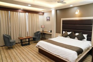 A hotel room with a large bed, two armchairs, a small table, a desk, and a lamp.