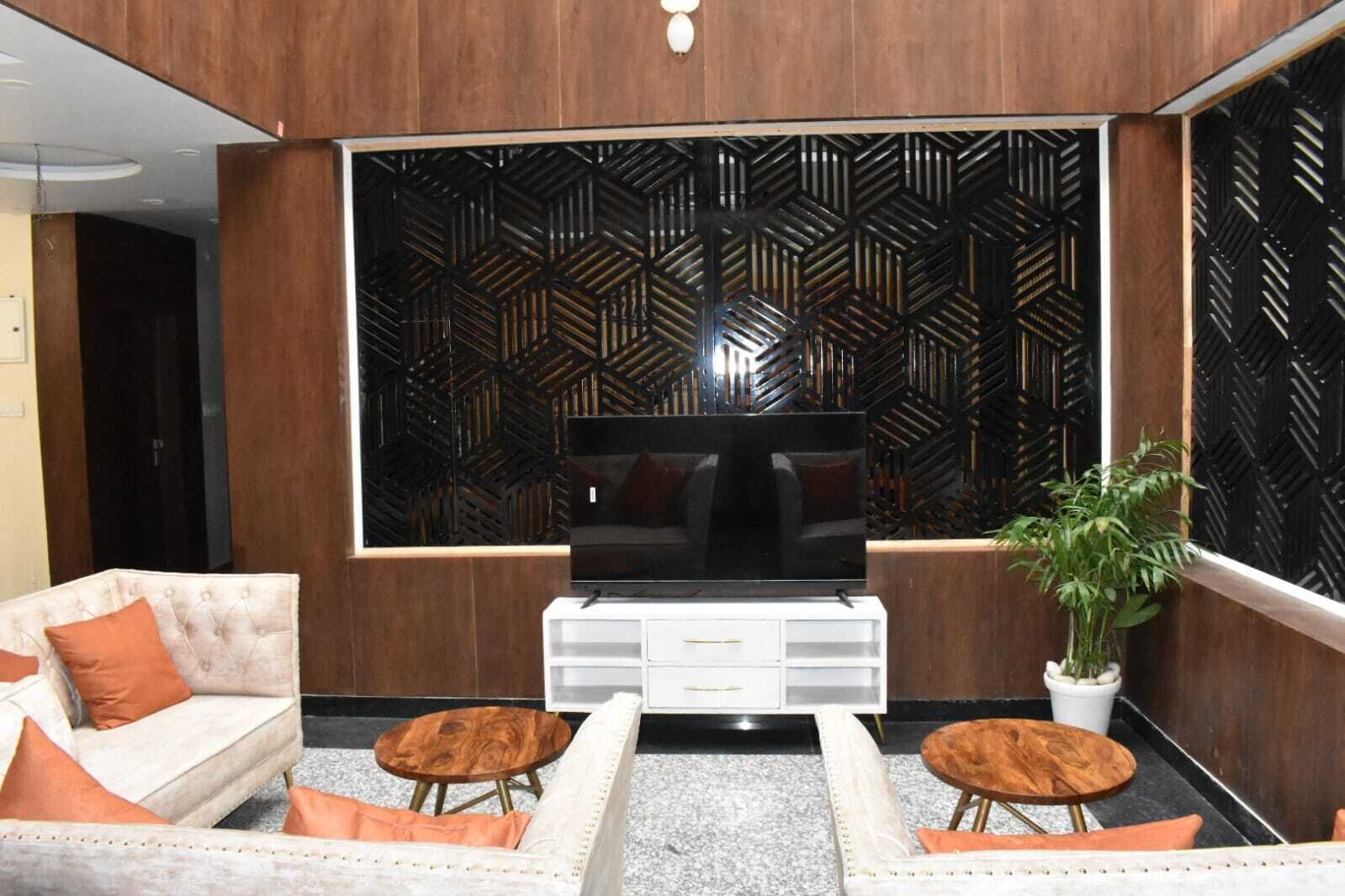 A modern living room with a large flat-screen TV, two sofas with orange cushions, a white entertainment unit, and a decorative wall panel.
