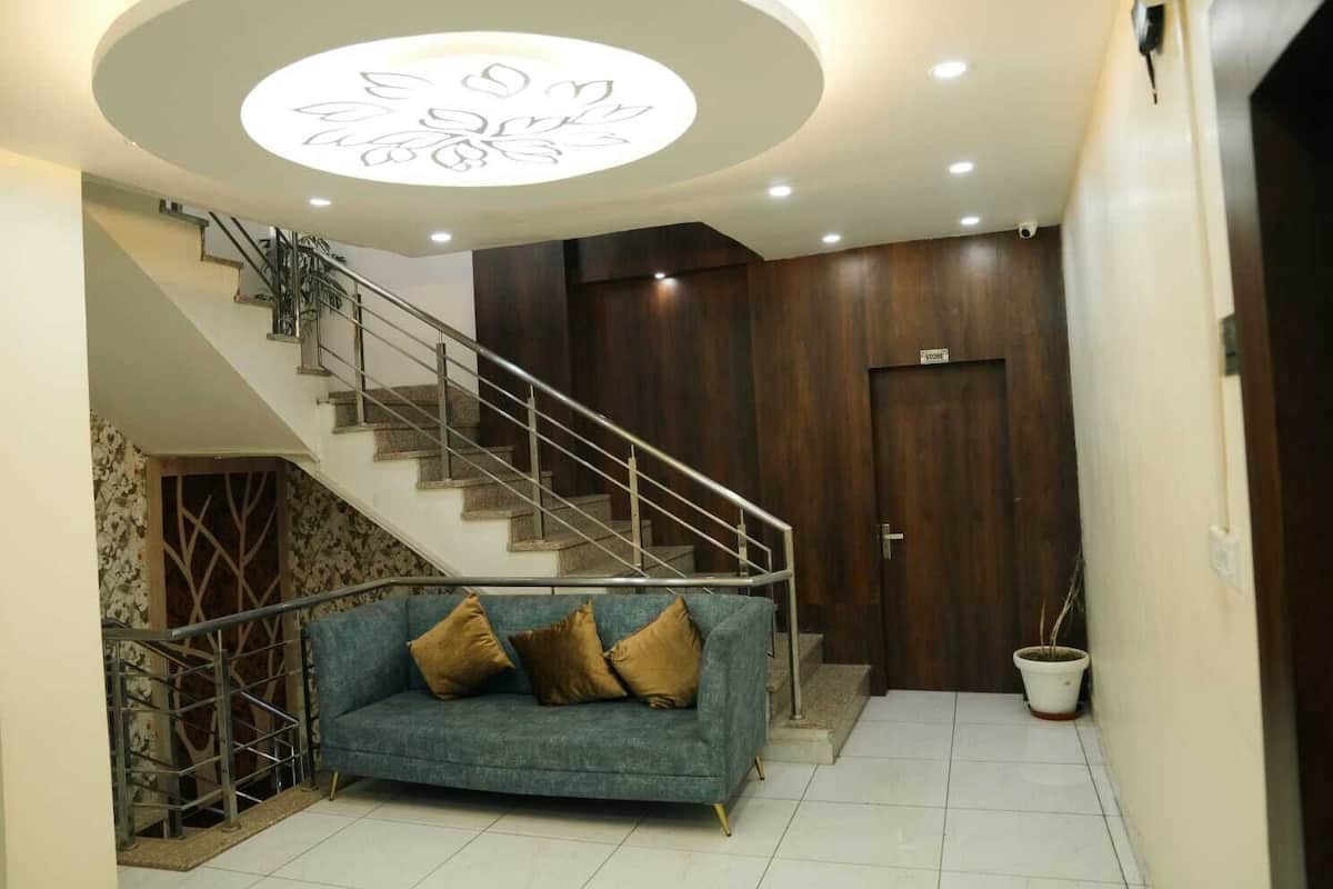 Una escalera con barandilla de metal que conduce a una puerta de madera, un sofá azul con cojines, y una lámpara circular en el techo.