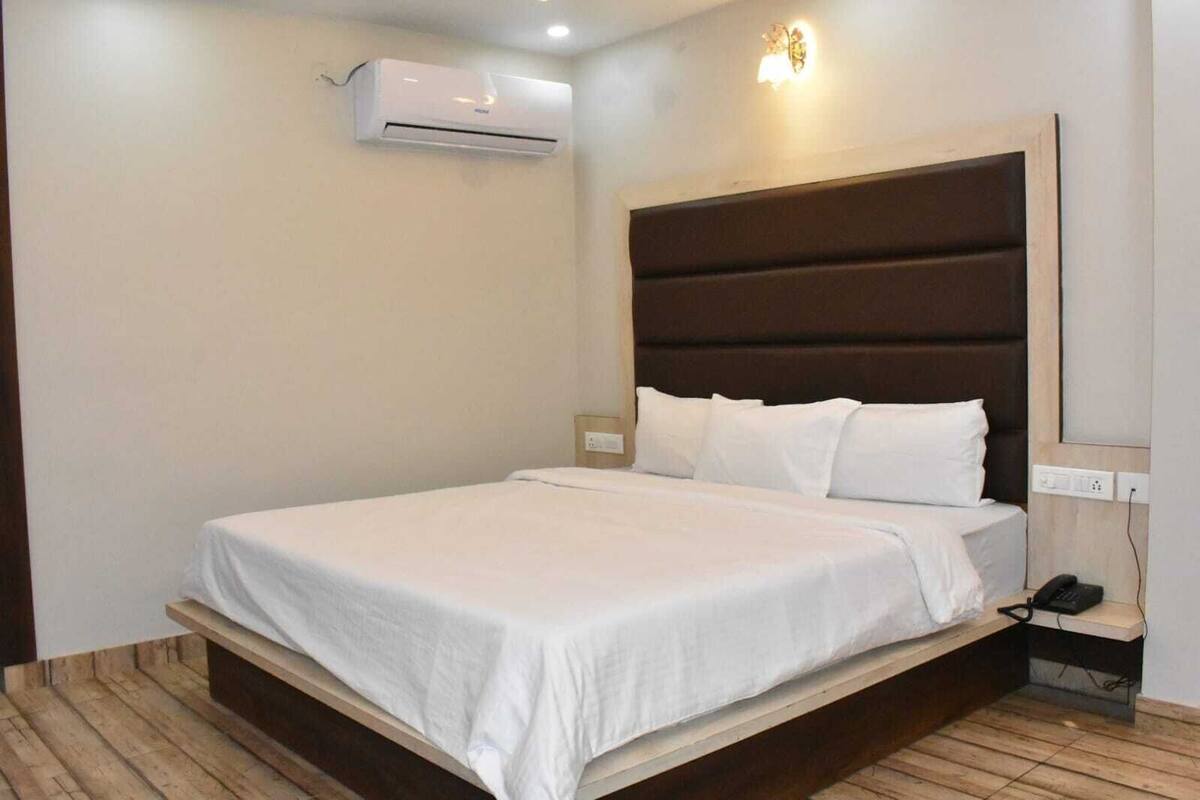 Habitación de hotel con cama, aire acondicionado de pared, teléfono en la mesita de noche y lámpara.