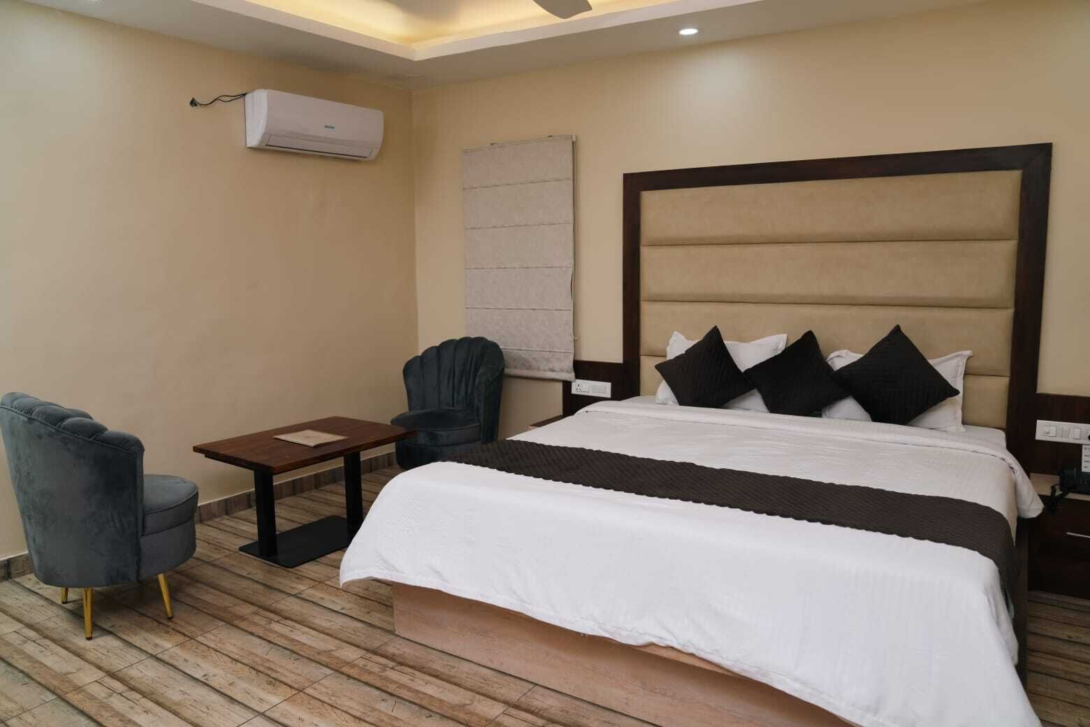Una habitación de hotel con una cama, una silla, una mesita pequeña y un equipo de aire acondicionado.