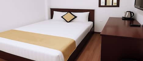 A neatly made bed with a white and gold bedspread, a wooden headboard, and a small bedside table with a kettle and a phone.