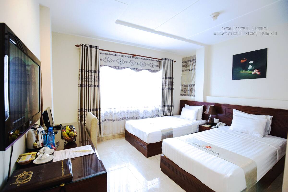 A hotel room with two beds, a desk with a computer, a television, and a window with curtains.