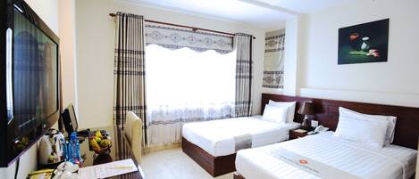 Habitación de hotel con dos camas, un escritorio con computadora, televisión y ventana con cortinas.