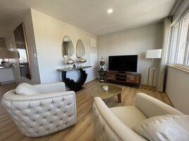 Una sala moderna con sofá, sillón y televisor sobre un mueble de madera.