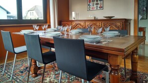 A dining room with a wooden table set for four, surrounded by chairs, a patterned rug, and a window with curtains. - Gîte Familial Avec Jardin et Garage Clos (OBERENTZEN)