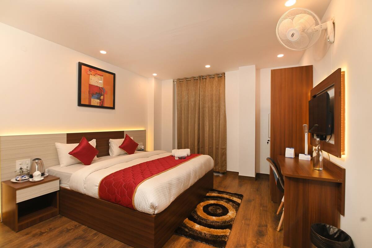 A hotel room with a bed, bedside table, desk, chair, and a television.
