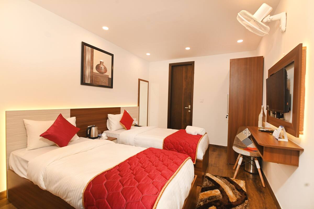 A hotel room with two beds, a desk, a chair, a mirror, a picture on the wall, and a ceiling fan.