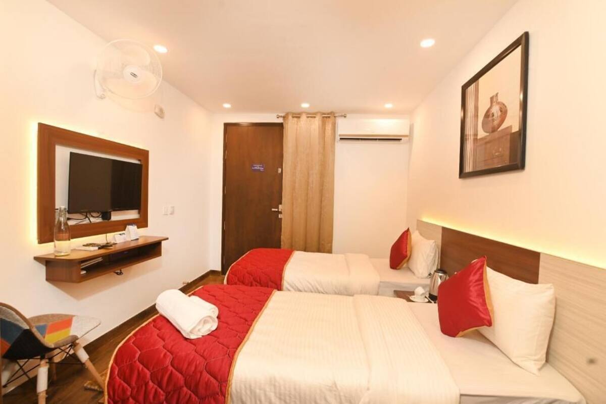 A hotel room with two beds, a television, a mirror, a ceiling fan, and a door.