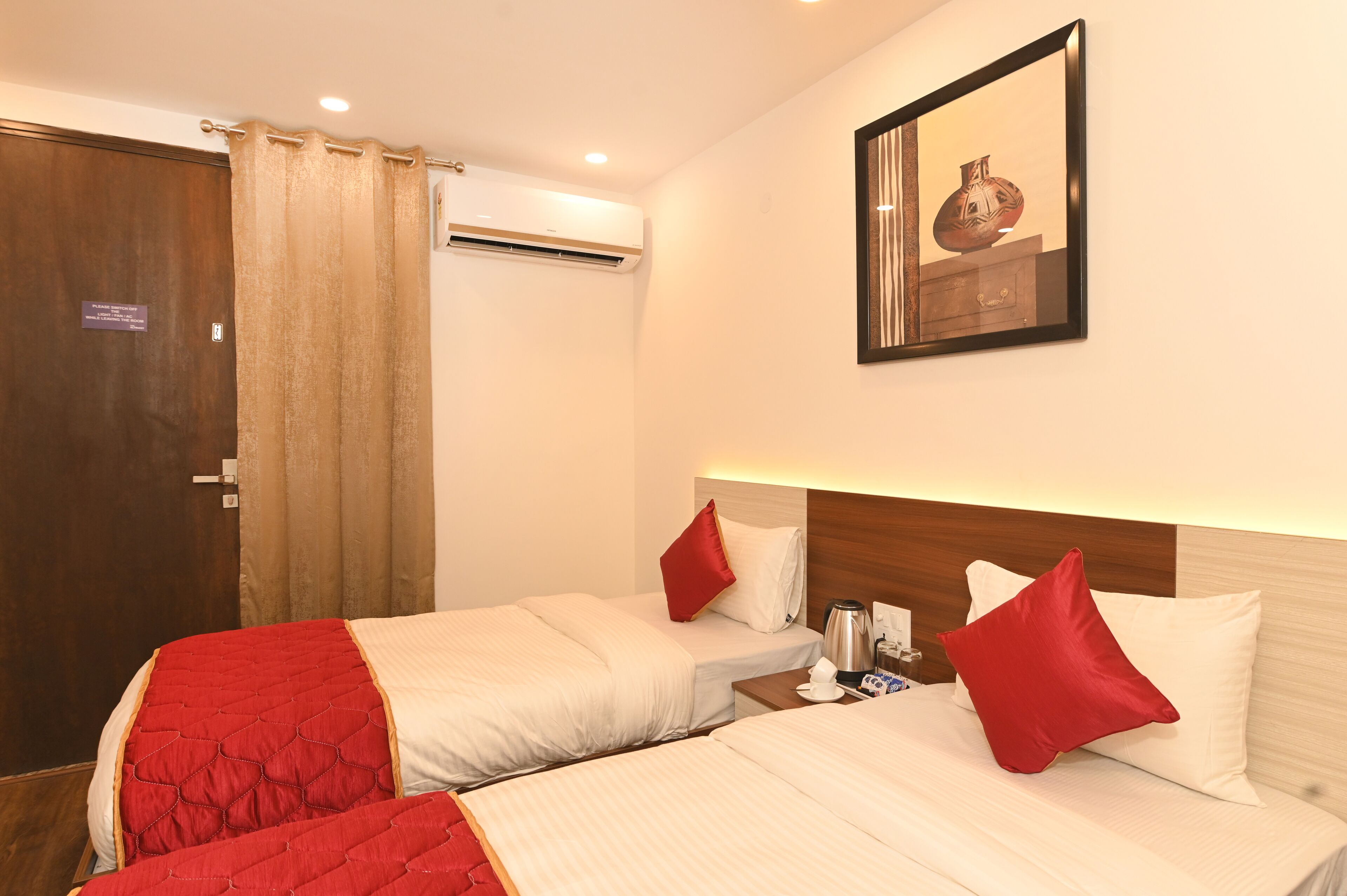A hotel room with two beds, each with red and white bedding, a wooden headboard, and a wall-mounted picture.