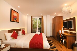 Habitación de hotel con cama, escritorio, televisor y ventana con vista a follaje.