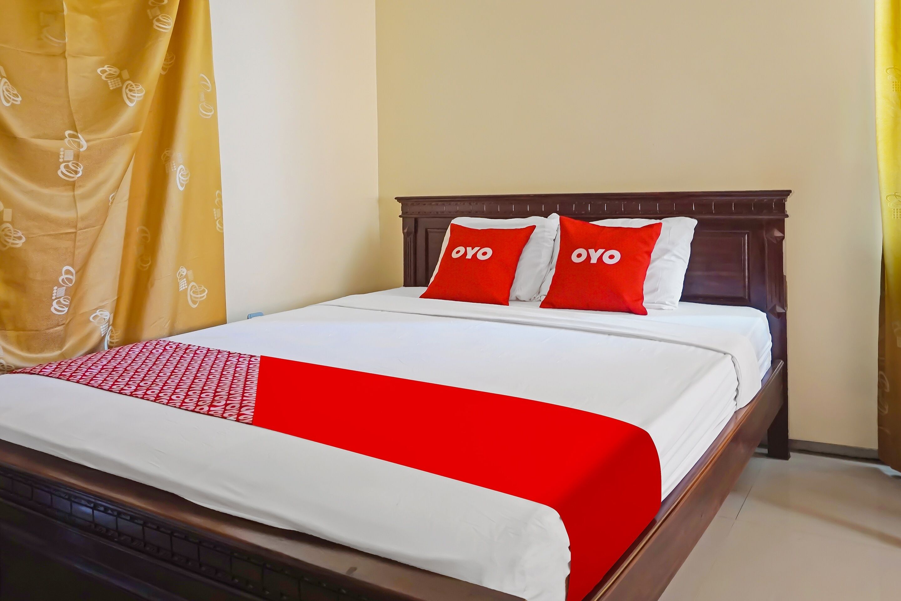 A neatly made bed with a white and red bedspread, two red pillows with the word "OYO" on them, and a wooden headboard.