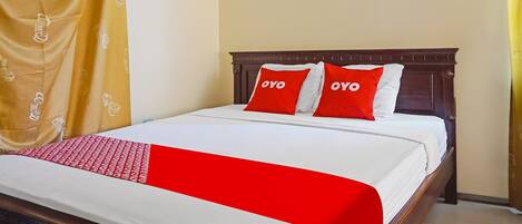 A neatly made bed with a white and red bedspread, two red pillows with the word "OYO" on them, and a wooden headboard.