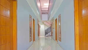 Um corredor com portas de madeira, piso de azulejos e uma escadaria ao longe.