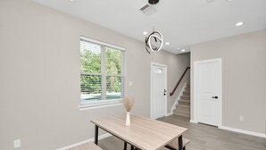 A spacious room with a large window, a dining table with benches, a staircase, and a door.