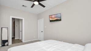 A bedroom with a bed, a ceiling fan, a TV on the wall, and a door leading to another room.