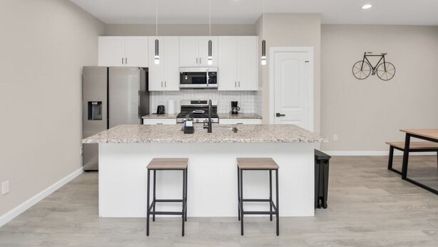 A modern kitchen with white cabinets, a central island with stools, and a bicycle mounted on the wall.