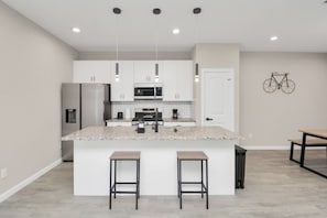 Una cocina moderna con armarios blancos, una isla central con taburetes y una bicicleta colgada en la pared.