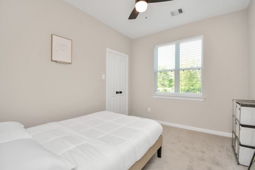 A bedroom with a bed, a ceiling fan, a window, and a door.
