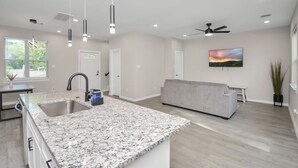 A modern kitchen with granite countertops, a built-in sink, pendant lighting, and a ceiling fan.