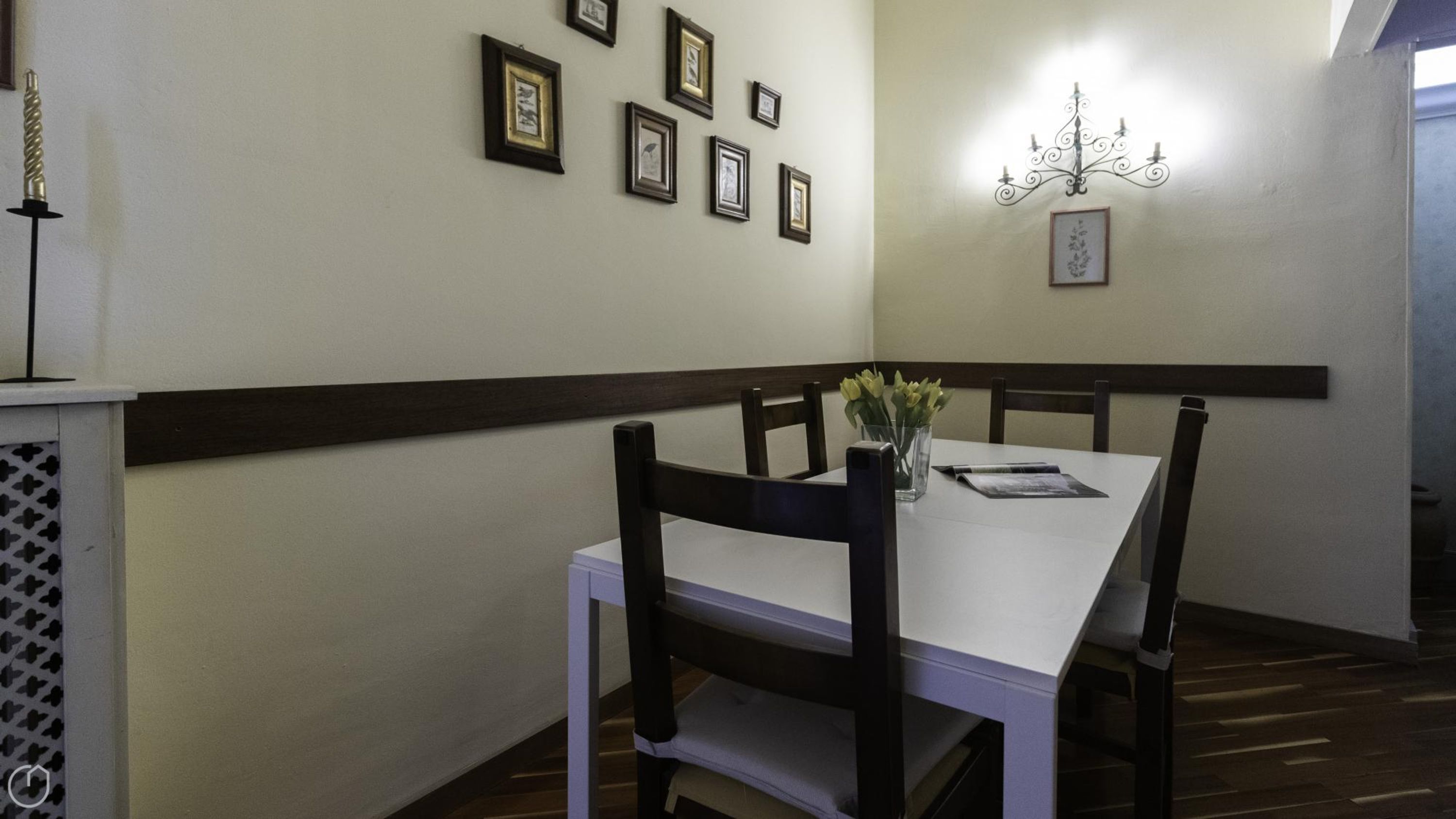 A dining area with a white table and dark wooden chairs, framed pictures on the wall, and a chandelier.
