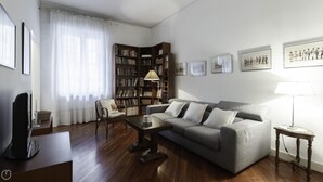 A living room with a grey sofa, a wooden coffee table, a bookshelf, and a television. - Dupr 5 (Milan)