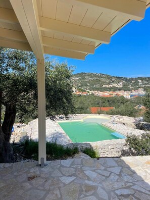 A stone pool with a pergola overhead, surrounded by olive trees and a view of a hillside town. - Bibi - Danilia Cottages (Paxos)