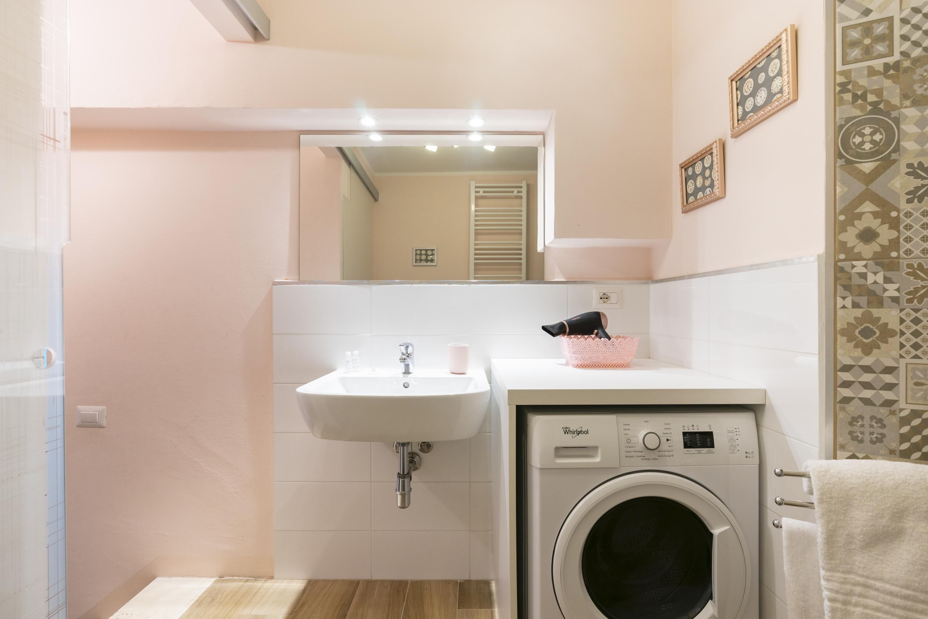 A bathroom with a sink, mirror, and washing machine.