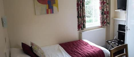 A bedroom with a bed, a TV on a stand, a radiator, and a window with curtains.