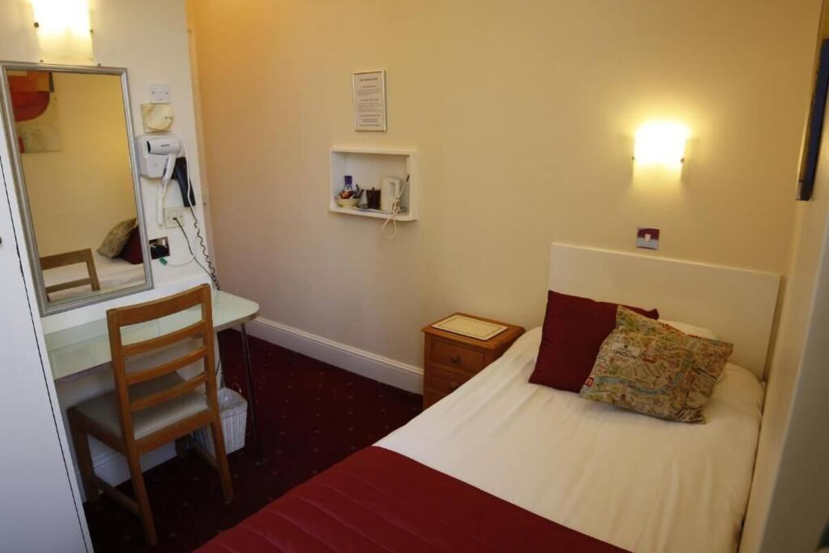 Une chambre d’hôtel comprenant un lit, un bureau avec une chaise, une table de chevet, un miroir, un téléphone fixé au mur, une étagère avec des articles de toilette et un oreiller en forme de carte.