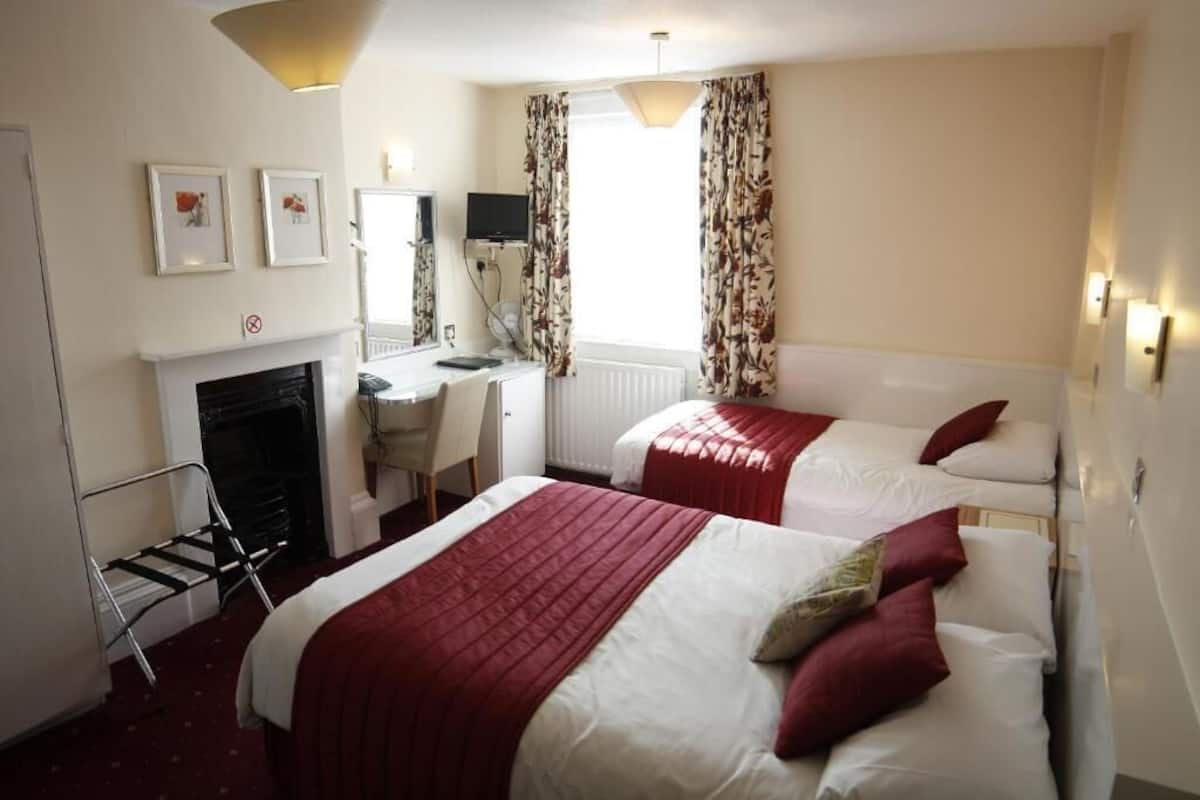 Une chambre d’hôtel avec deux lits, un bureau, une chaise, une cheminée et un téléviseur.