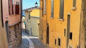 A narrow cobblestone street flanked by historic buildings with stone walls and wooden shutters. - Apartment with beautiful lake view (Gardone Riviera)