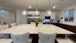 Una cocina moderna con una isla grande, armarios blancos, electrodomésticos de acero inoxidable e iluminación colgante.
