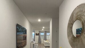Un pasillo con suelo de madera, un comedor con mesa y sillas, una zona de cocina y una sala de estar con sofá.