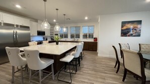 Una cocina moderna con una isla central, electrodomésticos de acero inoxidable, iluminación colgante y un ventanal grande.
