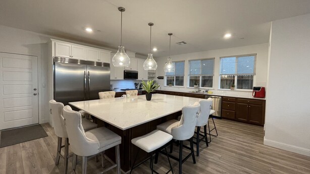 Una cocina moderna con una isla central, armarios blancos, electrodomésticos de acero inoxidable e iluminación colgante.