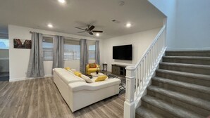 Una sala de estar moderna con un sofá, un sillón amarillo, un televisor de pantalla plana y una escalera.
