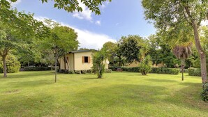 Une maison avec un petit jardin, entourée d’arbres et sous un ciel dégagé.