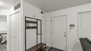 Un pasillo con puertas blancas, un banco, un perchero y una lámpara fijada a la pared.